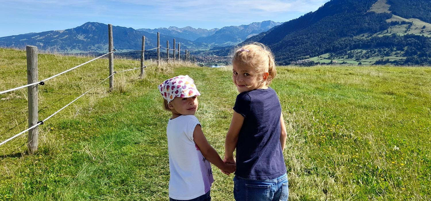 Zwei Kinder auf Bergtour im Oberallgäu mit Blick auf die Berge und See